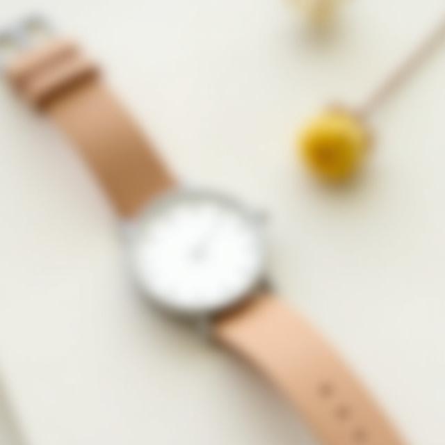 A minimalist Chamomile Classic watch with a simple white dial and a light brown strap.